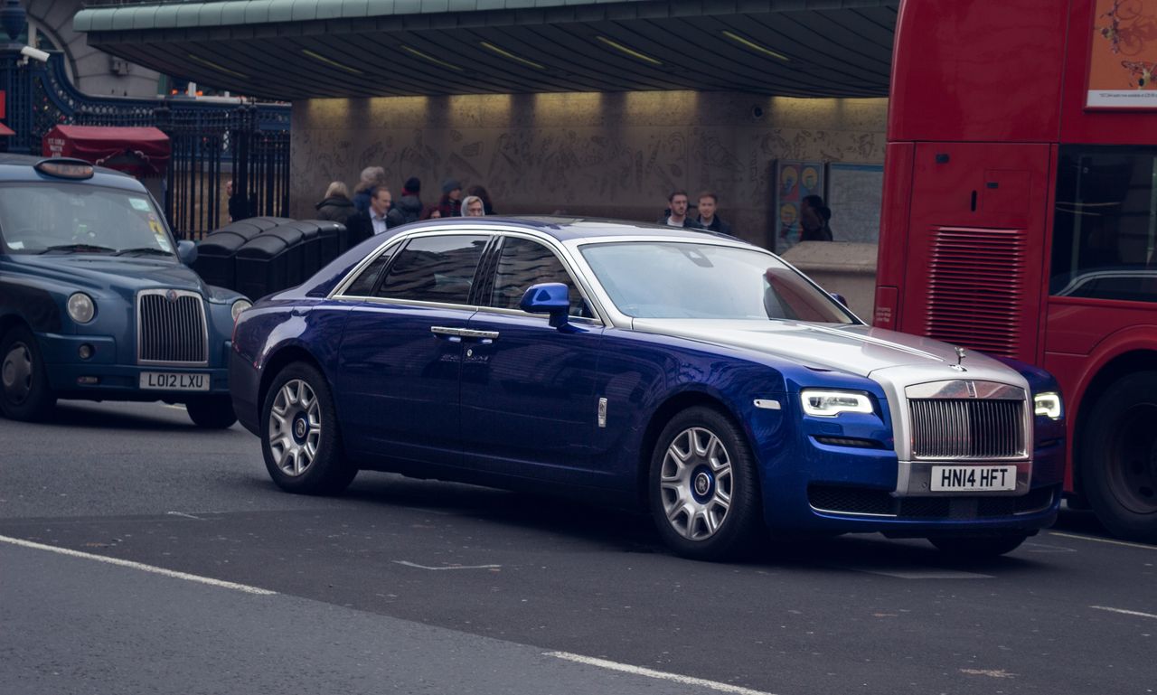 services-02 A blue luxury car driving on a busy street in London, surrounded by iconic vehicles.